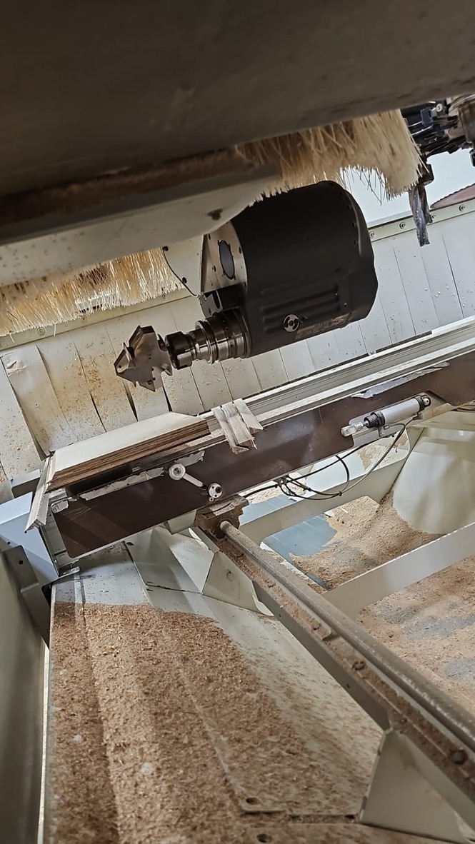 Detail vřetena CNC obráběcího centra SCM při frézování dřevěného panelu s odletujícími pilinami